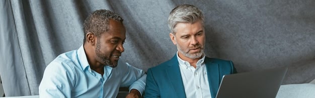A sales manager is giving constructive feedback to a team member while looking at performance data on a laptop. Both are engaged in a respectful and collaborative discussion.