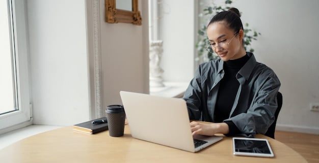 A person sitting at a desk, smiling and looking attentively at a laptop screen that displays their LinkedIn profile page. The profile features a professional headshot, a concise headline, and a summary highlighting their sales expertise. The background is a bright, modern office space.